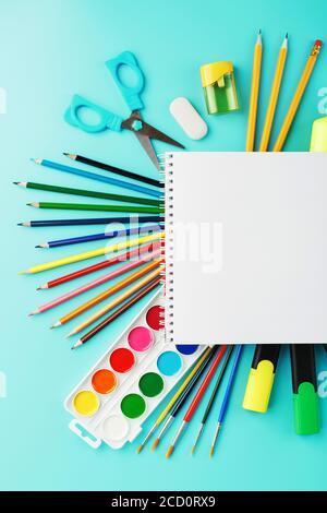 An album for creative development at school, with stationery on a cyanide background. A palette of colored paints, markers, brushes and pencils. Stock Photo