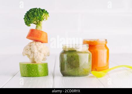 Natural baby food concept. Vegetable puree in jars near pyramid of brocolli, carrot, cauliflower and zucchini pieces on white background with blank sp Stock Photo