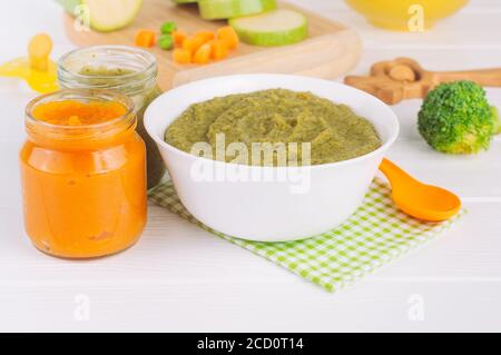 Natural baby food concept. Vegetable broccoli and carrot puree in the plate and jar on the light wooden background near ingredients. Selective focus. Stock Photo