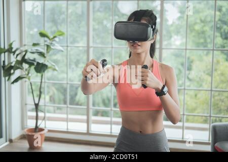 Workout at home. Young woman wearing VR headset doing working out interacting with 3d simulation at home. Stock Photo