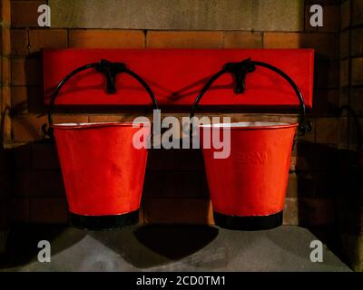 Vintage fire buckets hanging on hooks attached to brick wall Stock Photo