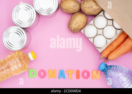 Food donation for the needy on a pink background top view. Potatoes, carrots, water, sunflower oil, eggs and canned food. Stock Photo