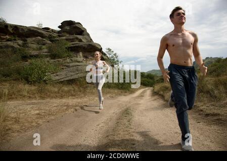 A guy and a girl in sportswear run along a mountain road Stock Photo