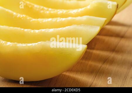 Row of sweet juicy honeydew melon slices on a brown wood cutting board. Sweet fruits and berries. Vegetarian, raw food diet and healthy eating. Stock Photo
