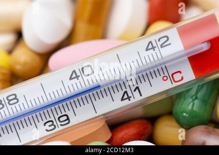 Thermometer indicating a temperature above 40 °C. Background of tablets and pills of different kinds and colors