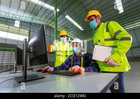 Asian Supervisor engineer Consult with warehouse workers, Inside the Heavy Industry Factory male Industrial Engineer Works on Personal Computer in the Stock Photo
