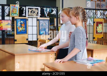 Two Schoolgirls with pigtails are standing in the classroom at the Desk Stock Photo