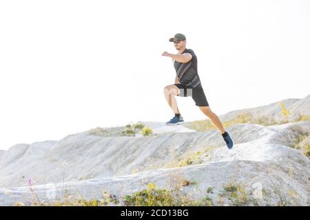 Young sporty runner man jumping from the hill on trail running cross Stock Photo