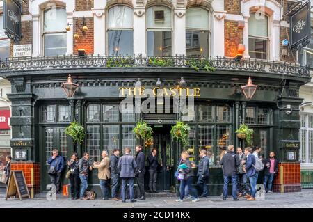 People drinking outside The Castle pub in Cowcross Street, London. Pawnbrokers sign refers to licence issued by King George IV in early 19th century. Stock Photo