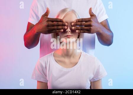 afro man closing her girlfriend's eyes and making surprise, Loving couple and relationship concept, love, isolated blue background, studio shot Stock Photo
