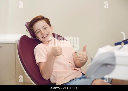 Dental clinic. Happy boy patient showing thumbs up sign during dentist visit Stock Photo