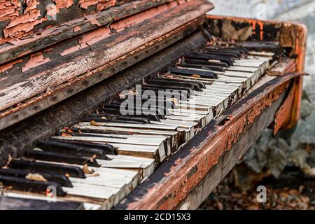 An old broken piano thrown into the street with peeling paint and leaves on the keys. Selective focus. Stock Photo