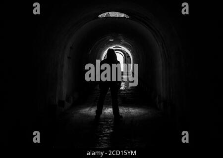 A lonely hooded man walks out into the light from a dark, abandoned underground corridor in fort Pospelova, Vladivostok.