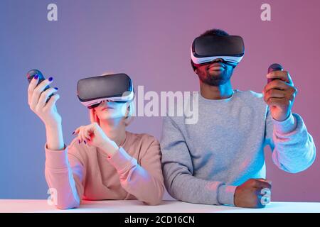 young attractive people concentrated on playing video games while sitting at the table, close up photo, studio shot, Stock Photo