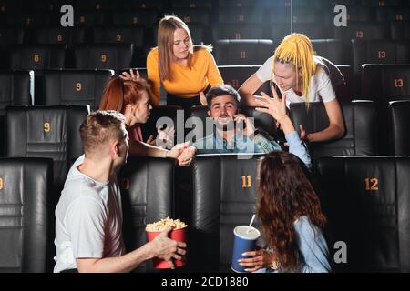 young people trying to explain their friend that it isn't allowed to talk on smart phone at the cinema. close up photo. selfish man doesn't care about Stock Photo