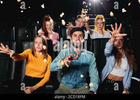 Dissatisfied multi racial friends watching film, throwing popcorn to the screen , sitting in the cinema. negative feeling and emotion, frustration Stock Photo
