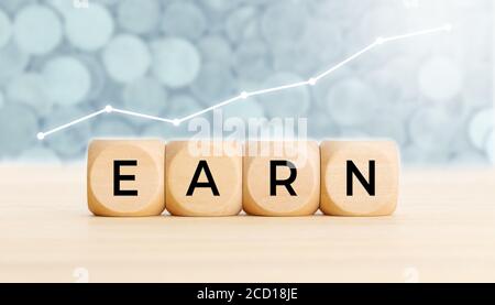 Earn concept. Wooden blocks with text on table and chart at background. Copy space Stock Photo