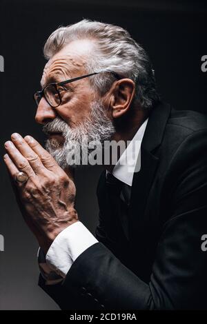 Head portrait of senior caucasion well-groomed businessman in spectacles wearing posing in profile isolated over black background Stock Photo