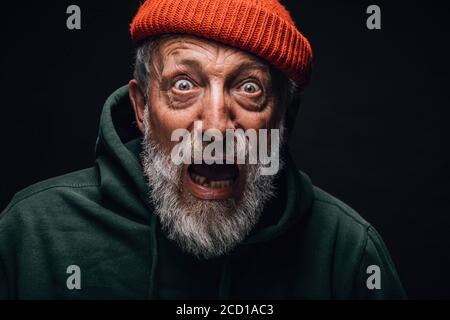 Frightened shocked bearded elderly man stares at camera with open mouth and bugged out eyes, bated breath, seen smth he was scared of, isolated over b Stock Photo