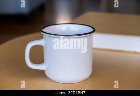 Coffee mug mockup on a wooden table. White color blank cup with handle for hot beverage, blurred background. Advertise, branding template Stock Photo