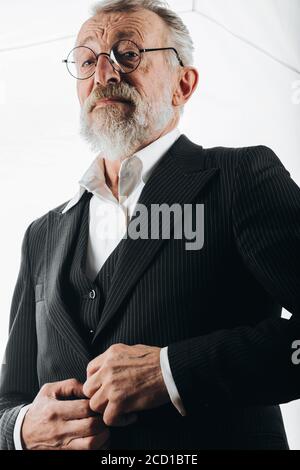 Confident serious senior male loyer in round spectacles and formal elegant suit looking at camera with wise expression, isolated over white background Stock Photo