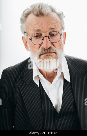 Pensive bearded grey haired stylish elderly business man in formal black suit, no tie, being deep in thoughts, looks aside, isolated over dark Stock Photo