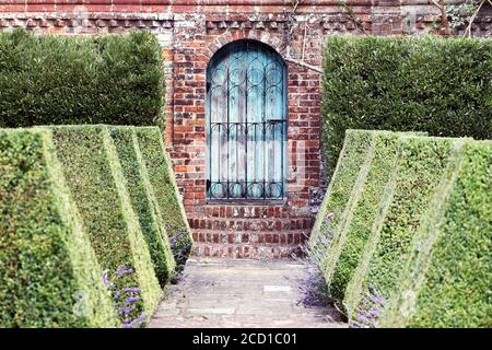 Old garden gate in a brick garden wall with neat box topiary hedging Stock Photo