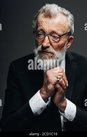 Tired serious senior male loyer in round spectacles and formal elegant suit thinking about difficult case over dark background Stock Photo