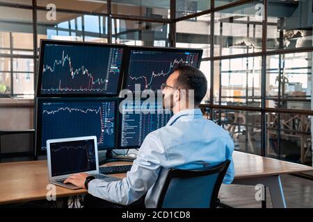 Stock Traiding. Trader sitting at office analyzing price flow on digital screen browsing laptop monitoring market concentrated back view Stock Photo