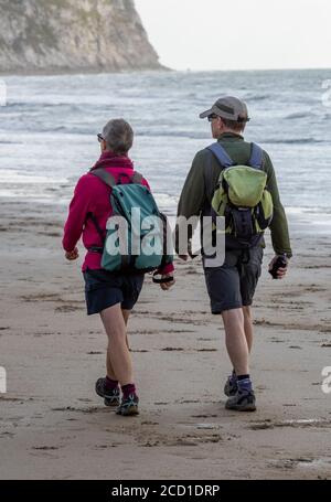 an older or middle aged couple wearing walking gear or clothes walking along a beach at yaverland on the isle of wight. Stock Photo