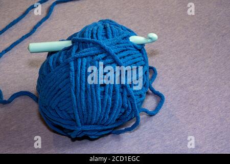 A plastic crochet hook is pushed through a large ball of thick blue yarn meant for making blankets. Stock Photo