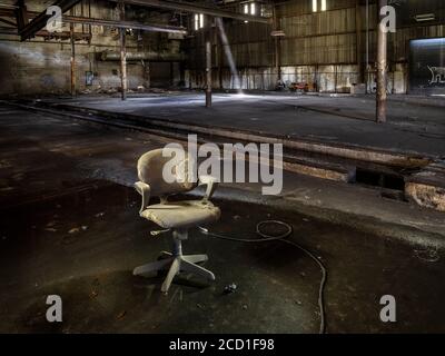 Old dirty chair sitting in water inside abandoned industrial factory Stock Photo