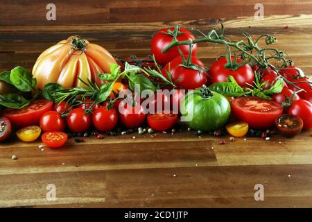 various colorful tomatoes and basil leaves on rustic table. fresh delicious zebra tomato and ccor de boeuf Stock Photo