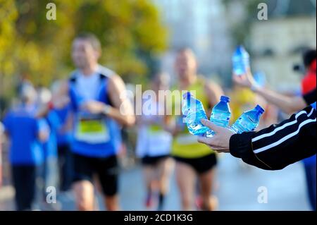 hand with 3 small bottles of water offering water to runners at a marathon refreshment. Selective focus Stock Photo