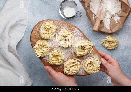 Tagliatelle. In women's hands a wooden Board with traditional Italian homemade raw uncooked pasta. Selective focus Stock Photo