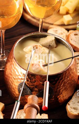 Gourmet Swiss fondue dinner on a winter evening with assorted cheeses on a board alongside a heated pot of cheese fondue with forks dipping bread Stock Photo