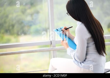 Smiling business woman sitting at desk with laptop and writing something in office Stock Photo
