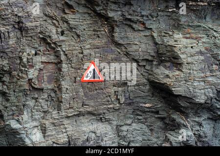 Sign warning of falling rocks from a cliff face due to erosion Stock Photo