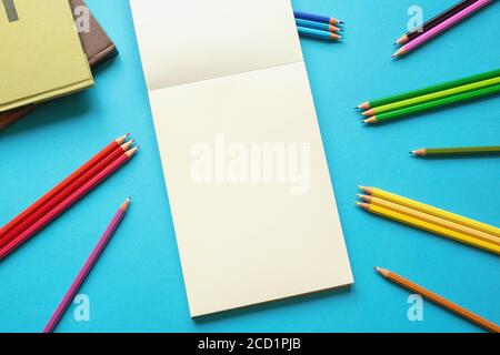 School concept. Colorful colored pencils, books and open sketchbook on blue paper background. Flat lay, free space for text or picture Stock Photo