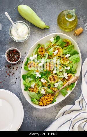 Delicious fresh lettuce salad with grilled zucchini, corn and soft goat cheese with spices and olive oil. Selective focus, top view Stock Photo