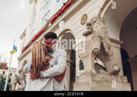 Happy couple in love walking in old Lviv city wearing traditional ukrainian shirts. People hug by town hall lion Stock Photo