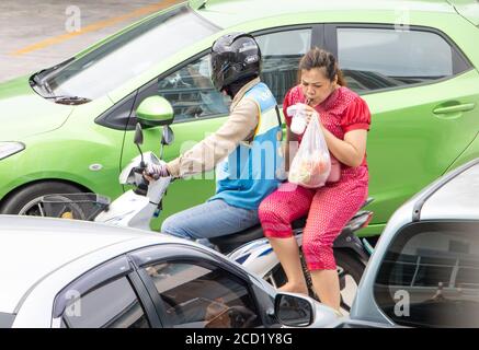 SAMUT PRAKAN, THAILAND, JUL 03 2020, A taxi driver on a motorcycle rides with a drinking woman. The mototaxi driver carry a passenger between cars on Stock Photo