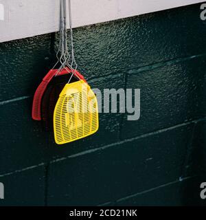 Plastic mesh fly swatters with lightweight wire handle hanging on a wall in an outdoor patio diner for use by staff or customers to kill flies. Stock Photo