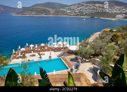 The swimming pool and sun decks of the Zest beach club in Kormuluk with the town of Kalkan, Turkey,  in the background. Kalkan is a popular holiday de Stock Photo