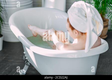Beautiful young woman pampering her body in water, taking bath with mineral oils in relaxing atmosphere of hotel spa zone at sunny morning Stock Photo