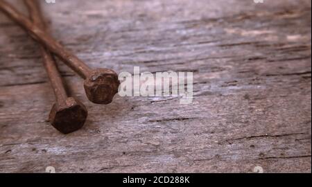 Two old rusty nails rest on a wooden background. Construction concept or religious theme. Stock Photo