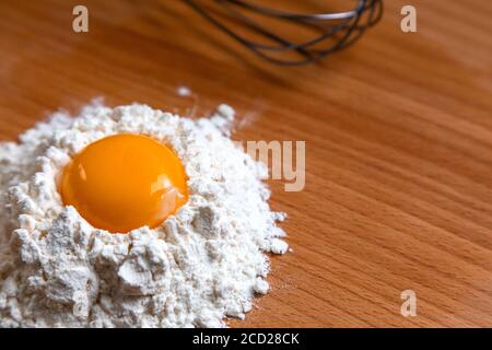 Cooking ingredients and kitchen tools on wood table. Close up egg yolk in flour Stock Photo