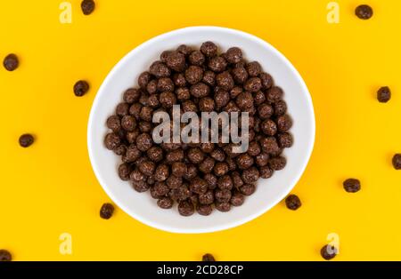 White bowl with chocolate corn cereal balls and milk on yellow background, top-down view. Modern fresh breakfast image. Stock Photo