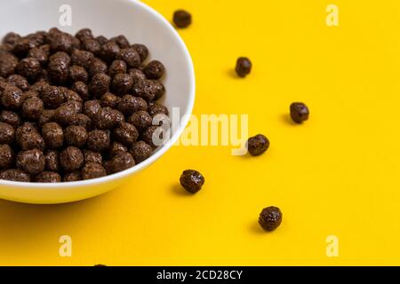 White bowl with chocolate corn cereal balls and milk on yellow background, top-down view. Modern fresh breakfast image. Stock Photo