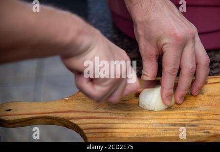 Human hands slicing onion onion on a wooden board for midday lunch. Food seasonings. Brazilian cuisine. Stock Photo
